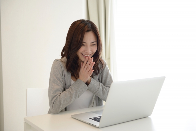 パソコンの画面を見て笑顔になるパーカーの女性
